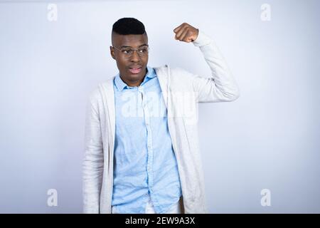 Junger schöner afroamerikanischer Mann in lässiger Kleidung, die Arme zeigt Muskeln lächeln stolz Stockfoto