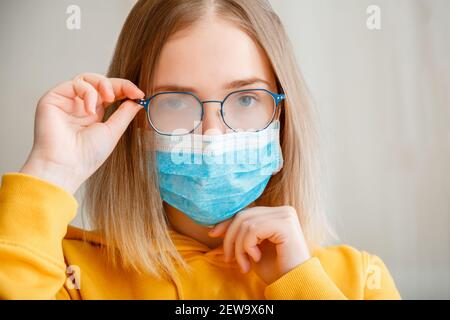 Neblige Brille trägt auf junge Frau. Teenager-Mädchen in blau medizinische Schutzmaske und Brillen wischt verschwommen neblig vernebelte Gläser. Neuer Normalwert Stockfoto