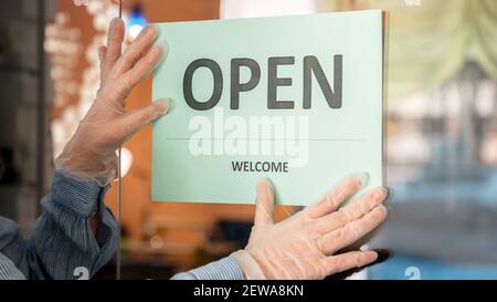 Green Sign Open Welcome covid 19 Lockdown wieder als neu normal. Schild zum Wiederöffnen am Eingang der Eingangstür öffnen. Frau in schützenden medizinischen Handschuhen hängt O Stockfoto