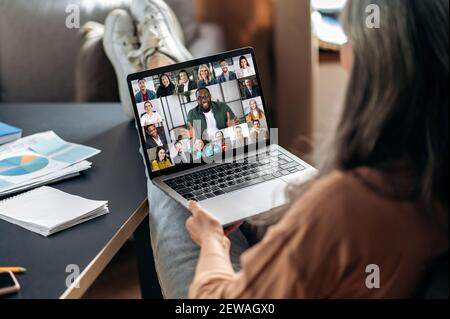 Online-Briefing. Stilvolle moderne reife grauhaarige Frau kommunizieren mit Kollegen online per Videoanruf nutzt App und Laptop, sitzen in ihrem Home-Office, werfen ihre Füße auf den Tisch Stockfoto