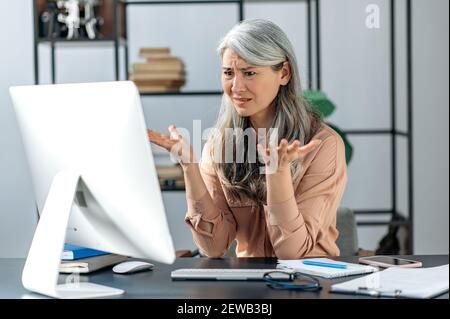 Verwirrt grauhaarige reife Dame, Geschäftsfrau Manager oder Berater, Blick auf den Computer in Verwirrung, erhielt eine unverständliche Nachricht, oder seltsame Nachrichten Stockfoto