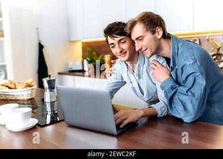 Zwei glückliche homosexuelle Jungs. Gay paar stehen an der Küche, verwenden Sie einen Laptop, im Internet surfen, einen Film ansehen, online einkaufen, Verbringen Sie Zeit miteinander Stockfoto