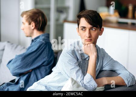 Streit zwischen einem schwulen Paar in der Liebe. Ein verärgerter Kerl und sein Partner sind beleidigt und ignorieren sich gegenseitig, während sie auf der Couch sitzen und sich in verschiedene Richtungen abwenden Stockfoto