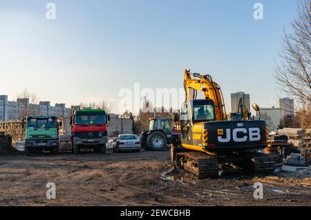 POZNAN, POLEN - Mär 30, 2018: JCB Bagger auf einem Bauplatz mit geparkten Lastwagen in der Nähe von Wohngebäuden Stockfoto