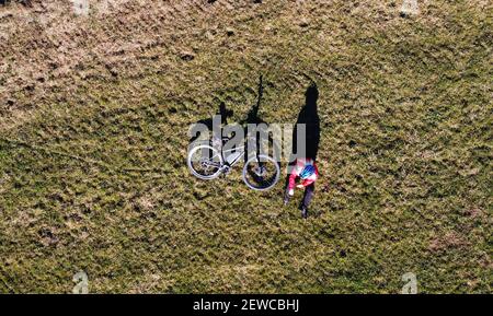 Luftaufnahme mit Drohne von Radfahrerin mit Fahrrad auf Wiese mit Licht und Schatten Stockfoto