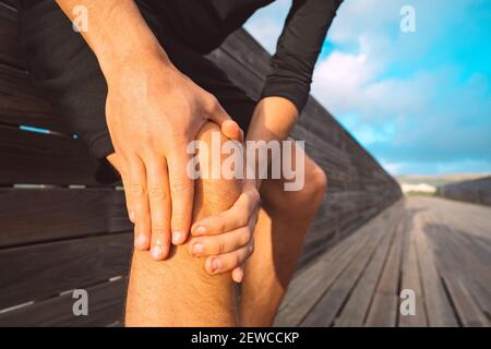 Mann, der unter Knieschmerzen im Freien leidet. Mann massiert sein Knie wegen Verletzung Stockfoto