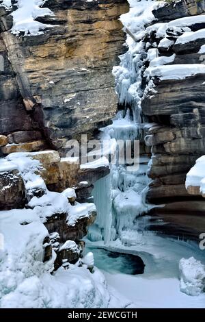 Ein vertikales Bild der Athabasca-Wasserfälle im Winter mit gefrorenem Eis, das sich an den Felswänden des Jasper National Park in Alberta, Kanada, festklammert. Stockfoto