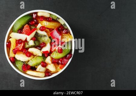 Frischer Obstsalatbecher aus saftigen Früchten auf schwarzem Hintergrund. Freier Speicherplatz für Text. Scheiben von frischen, saftigen und gesunden Früchten für eine gesunde Ernährung. Stockfoto