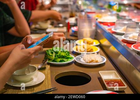 Menschen, die Smartphone beim Essen in Förderband Sushi-Restaurant Stockfoto