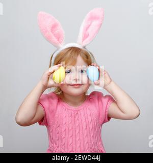 Schönes lächelndes kleines Mädchen trägt Osterhasen Ohren und hält Ostern gefärbte Eier auf weißen Wand Hintergrund. Stockfoto