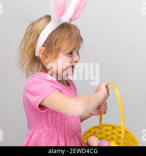 Schönes lächelndes kleines Mädchen trägt Osterhasen Ohren und hält Ostern Korb mit bunten Eiern. Osterfeiertage und Eiersuche. Stockfoto