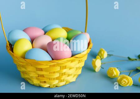 Ostereier im Korb mit kleinen Blumen beiseite und kopieren Platz auf blauem Hintergrund. Osterkomposition. Stockfoto