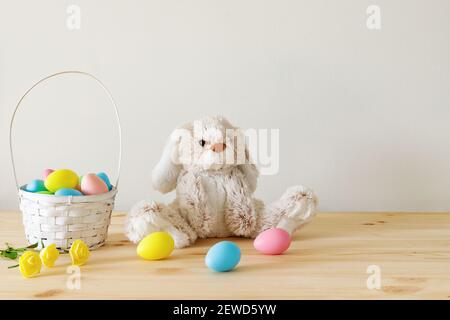 Osterspielzeug Hase, bunte Eier mit Korb auf Holztisch mit weißem Hintergrund und Kopierraum. Stockfoto