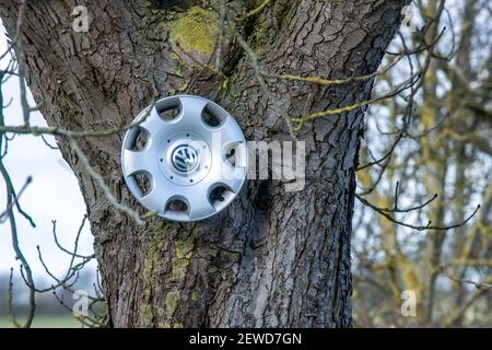 Gottesgabe, Deutschland. Februar 2021, 26th. An einem Baum hängt neben einer Straße mit zahlreichen Schlaglöchern ein gefallener Hubcap. Auto, das durch ein Schlagloch auf einer Straße fährt. Das eisige Wetter der letzten Wochen sorgt für durchbrochene Straßen mit tiefen Schlaglöchern. Quelle: Jens Büttner/dpa-Zentralbild/dpa/Alamy Live News Stockfoto