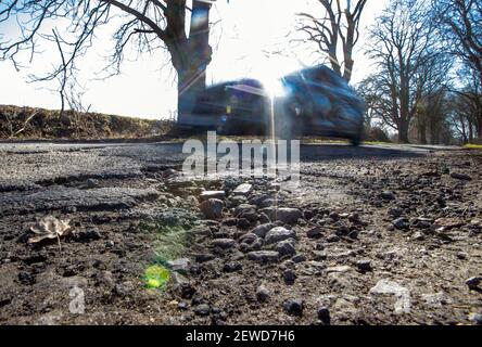 Gottesgabe, Deutschland. Februar 2021, 26th. Ein Auto fährt in einer Allee an einem Schlagloch vorbei. Das eisige Wetter der letzten Wochen sorgt für durchbrochene Straßen mit tiefen Schlaglöchern. Quelle: Jens Büttner/dpa-Zentralbild/dpa/Alamy Live News Stockfoto