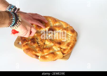 Scheiben von Ramadan Pita (Ramazan Pidesi) traditionelle türkische Brot für den heiligen Monat Ramadan auf weißem Hintergrund. Ramadan-Konzept. Mann's Hand schneiden Pita Stockfoto