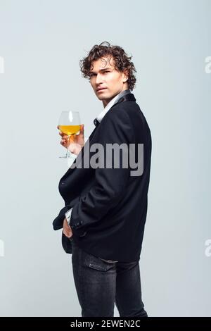 Selbstbewusster junger Mann in einer Jacke mit einem Glas Wein Auf weißem Hintergrund Stockfoto