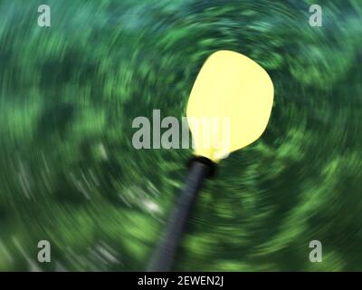 Verwischtes gelbes Blatt des Bootspadels. Radiale Bewegungsunschärfe des primären dunkelgrünen Wasserhintergrunds mit hellen grünlichen Farben. Stockfoto