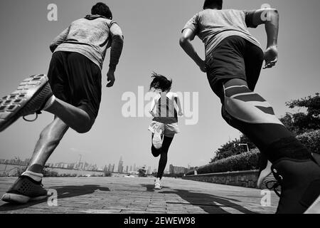 Drei junge asiatische Erwachsene joggen im Freien, hinten und in den tiefen Winkeln, schwarz und weiß Stockfoto