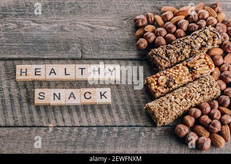 Müsliriegel und Mandeln, Haselnüsse. Alte Braune Holztisch Hintergrund. Holzbuchstaben Wörter Text gesunde Snack Bars. Draufsicht Stockfoto