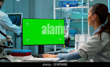 Forscher beim Blick auf Chroma-Key-Display in modern ausgestatteten Labor in der Nacht. Team von Mikrobiologen tun Impfstoffforschung Schreiben auf Gerät mit grünem Bildschirm, isoliert, Mockup-Display. Stockfoto