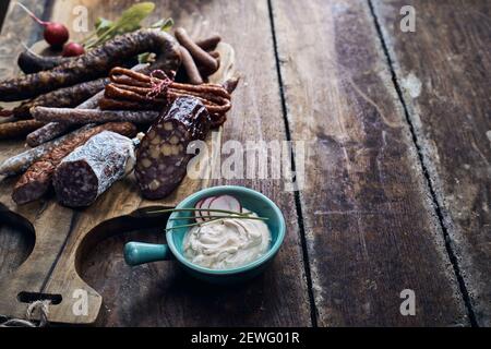 Von oben verschiedene leckere geräucherte und geräucherte Wildwürste Auf Schneidebrett neben cremigen Käse mit Rettich Scheiben und Schnittlauch Stockfoto