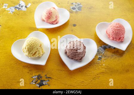 Hoher Winkel von verschiedenen Eisschaufeln mit cremiger Textur Auf herzförmigen Keramikplatten auf beschädigtem Tisch Stockfoto