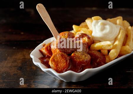 Nahaufnahme von appetitlich gegrillten gehackten Würsten mit Barbecue-Sauce serviert Mit Pommes frites und Mayo in Teller auf dunklem Holz Tabelle Stockfoto