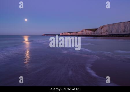 Monduntergang über Seaford Head und die sieben Schwestern vom Strand von Birling Gap an der Ostküste von Sussex im Südosten Englands Stockfoto