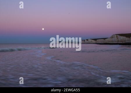 Monduntergang über Seaford Head und die sieben Schwestern vom Strand von Birling Gap an der Ostküste von Sussex im Südosten Englands Stockfoto