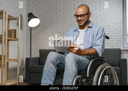 Behinderter junger afroamerikanischer Mann, der im Rollstuhl sitzt und benutzt Digitales Tablet Stockfoto