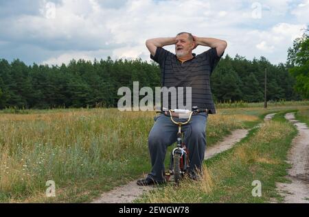 Alter Mann Stellen Sie sich vor, dass er jung ist, wenn er auf sitzt Kinderfahrrad Stockfoto
