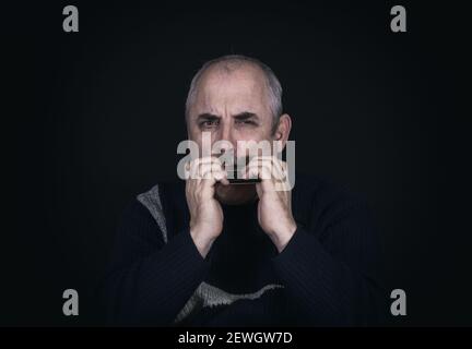 Nizza Low-Key-Porträt von reifen kaukasischen Mann spielen Mund Orgel Stockfoto