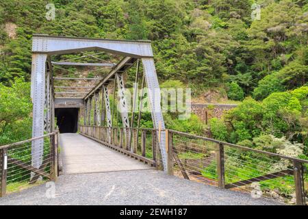 Eine alte Metalleisenbahnbrücke, die zu einem Tunnel in einer Klippe in der Karangahake Gorge, Neuseeland führt Stockfoto