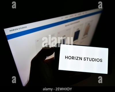 Person, die Smartphone mit Logo der deutschen Firma Horizn Studios (HS New Travel GmbH) auf dem Bildschirm vor der Website hält. Konzentrieren Sie sich auf die Telefonanzeige. Stockfoto