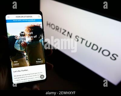 Person, die Mobiltelefon mit Website der deutschen Firma Horizn Studios auf dem Bildschirm vor der Business-Website. Fokus auf der Mitte des Telefondisplays. Stockfoto