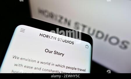 Person, die Mobiltelefon mit Website des deutschen Gepäckherstellers Horizn Studios auf dem Bildschirm mit Logo hält. Konzentrieren Sie sich auf die obere rechte Seite des Telefondisplays. Stockfoto