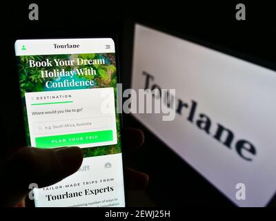 Person, die Smartphone mit Website des deutschen Online-Reisebüros Tourlane GmbH auf dem Bildschirm vor dem Logo hält. Fokus auf der Mitte des Handy-Displays. Stockfoto