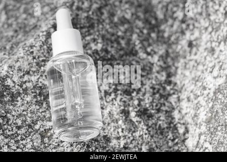 Transparente Flasche aus Serumglas mit Pipette auf Steinoberfläche. Natürliches organisches Wellness-Kosmetik-Konzept. Stockfoto