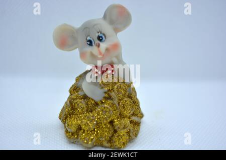 Keramik-Statuette einer niedlichen grauen Maus mit großen Ohren, die in einem Haufen von brassenden Goldmünzen steht. Stockfoto