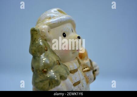 Weiße Keramikstatuette eines weihnachtlichen Teddybären in einem Weihnachtshut mit einem goldenen weihnachtsbaum und Geschenken in der Hand. Stockfoto