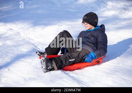 Lächelnder kleiner Junge, der auf dem Schlitten sitzt Stockfoto