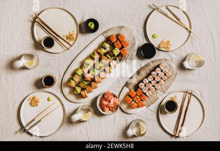 Absperrung Home Dinner Party mit japanischem Sushi von Lieferung oder Take Away Service. Flach-Lay von verschiedenen Lachs, Krabben, Garnelen, vegane Brötchen, Wasabi, Ingwer ana Zitronenwasser über hellem Hintergrund, Draufsicht Stockfoto