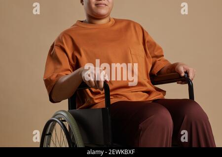 Cropped Porträt der zeitgenössischen gemischten Rasse Frau mit Rollstuhl, während Posiert im Studio vor neutralem Hintergrund Stockfoto