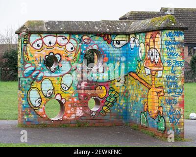 Mit Graffiti bedeckte Ziegelwand auf dem Kinderspielplatz im Greenspace Park, Westbury, Wiltshire, England, Großbritannien. Stockfoto