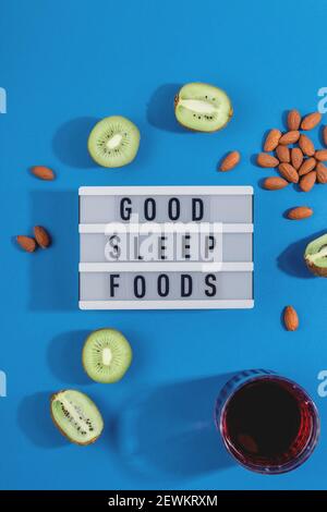 Behandeln Sie Schlaflosigkeit mit gesunden Schlaf Lebensmittel Mandeln, Kirschsaft und Kiwi. Layout auf blauem Hintergrund Stockfoto