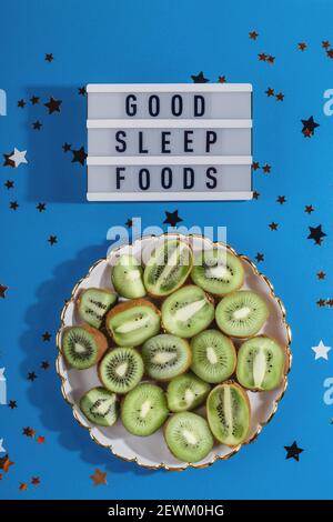 Ein Teller mit reifen Kiwi in Scheiben geschnitten auf blauem Hintergrund mit Sterne neben der Inschrift von guten Schlaf Lebensmittel Stockfoto