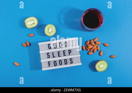 Behandeln Sie Schlaflosigkeit mit gesunden Schlaf Lebensmittel Mandeln, Kirschsaft und Kiwi. Layout auf blauem Hintergrund Stockfoto