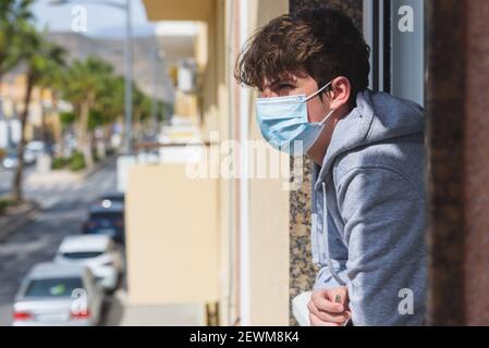 Alter älterer Mann in Schutzmaske gegen Virus schaut durch Fenster zu Hause bleiben für die Gesundheit. Stockfoto