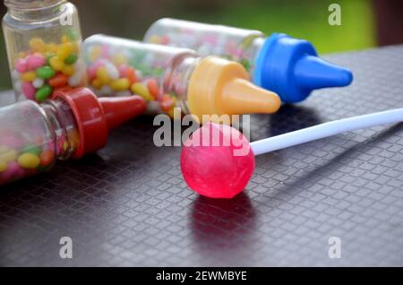 Der rosa Lollypop mit süßen Anisbohnen bunte Plastikflasche auf dem braun-grünen Hintergrund. Stockfoto
